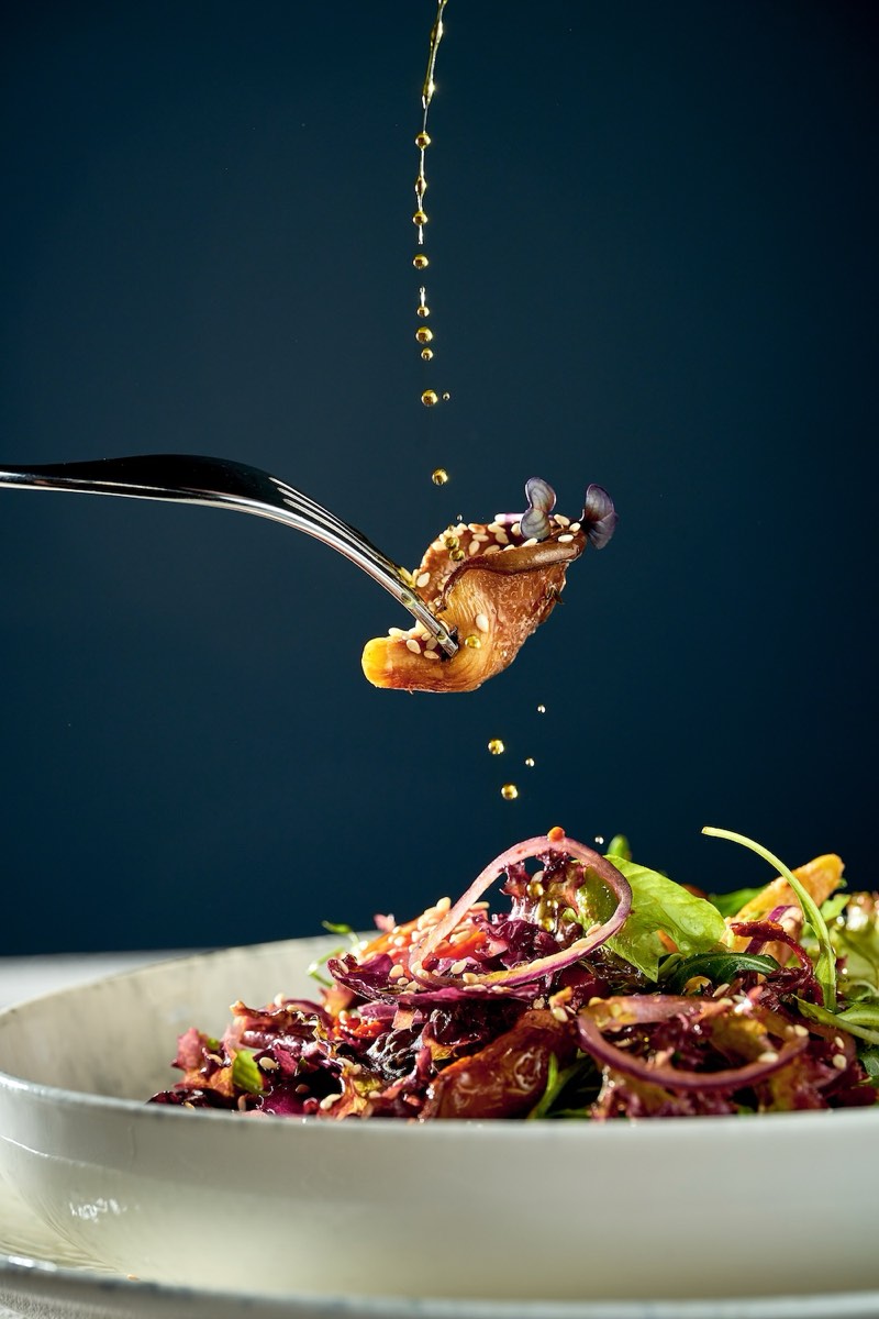A forkful of food held above a salad, with oil being drizzled